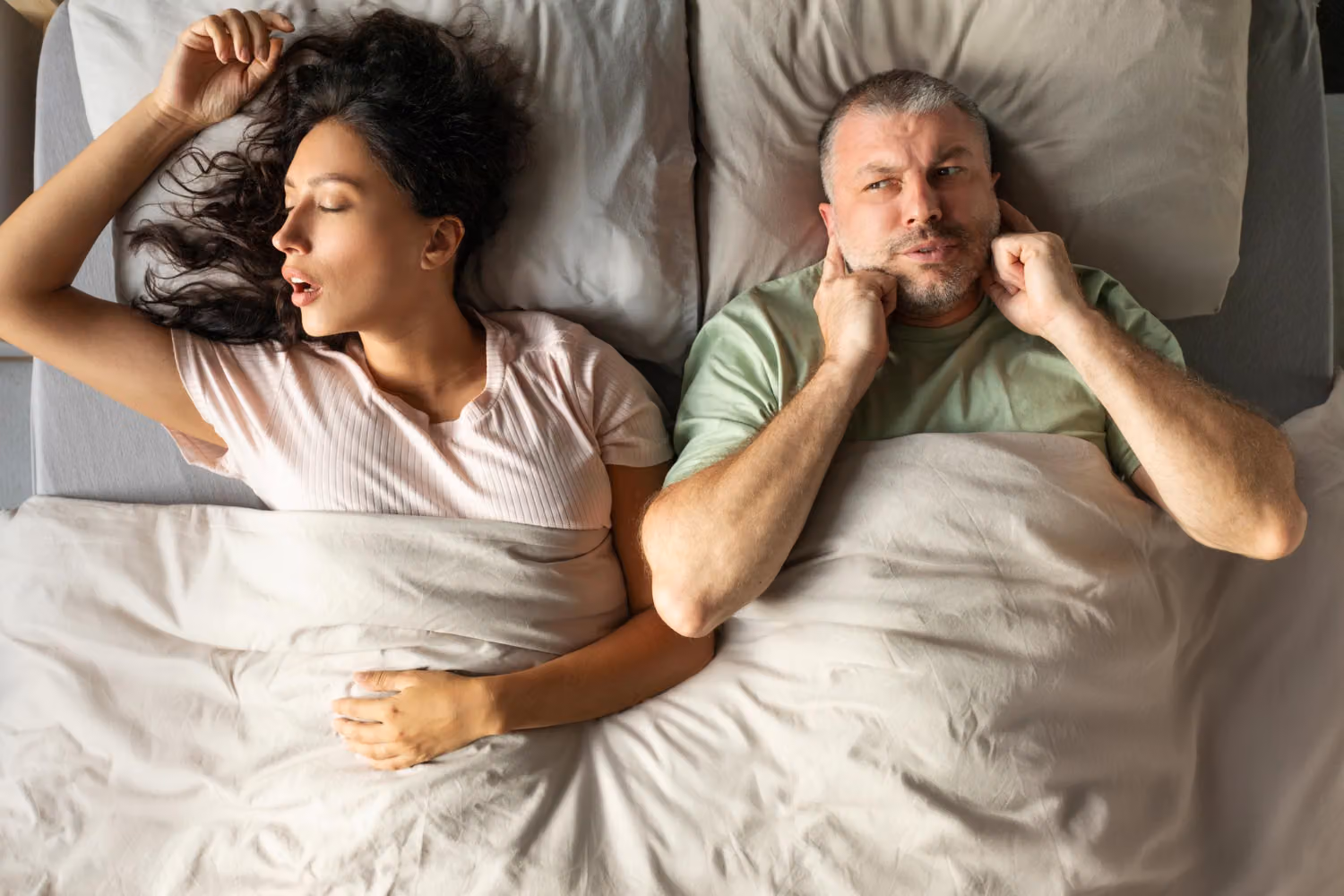 A man sleeps on his back with his mouth open, illustrating snoring and nighttime airway restriction.