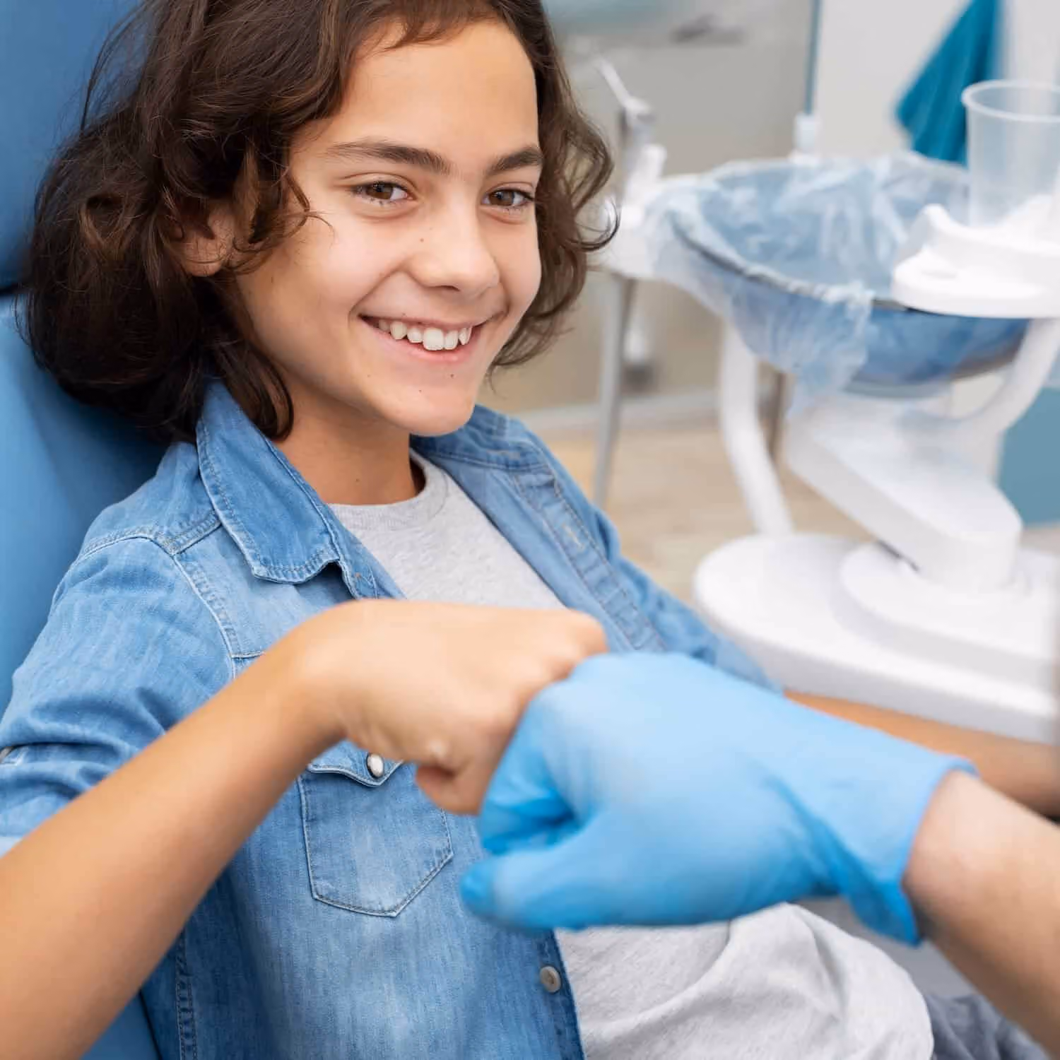 Pre-teen in a dental chair giving a fist bump to a gloved dentist hand