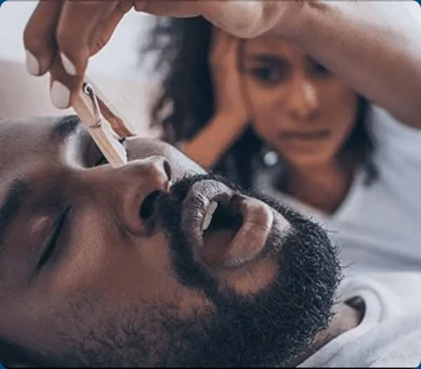 A clinician checks a sleeping patient’s airway while another person observes in the background.