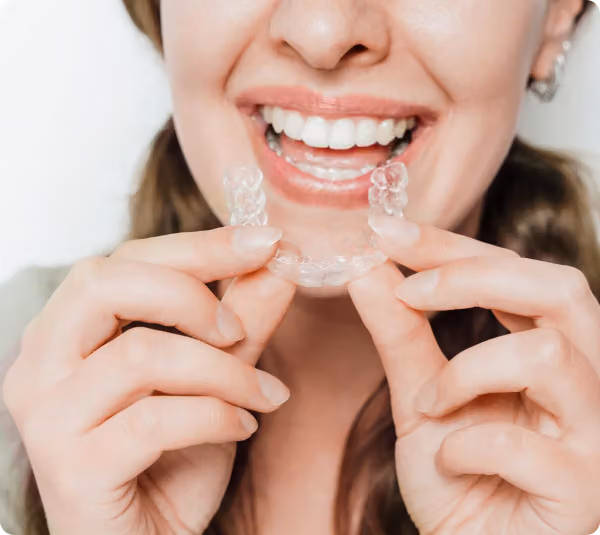 Smiling woman holding a clear retainer near her teeth.