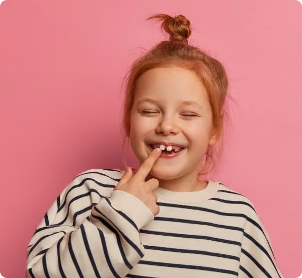 Smiling young girl with missing front teeth against a pink background.