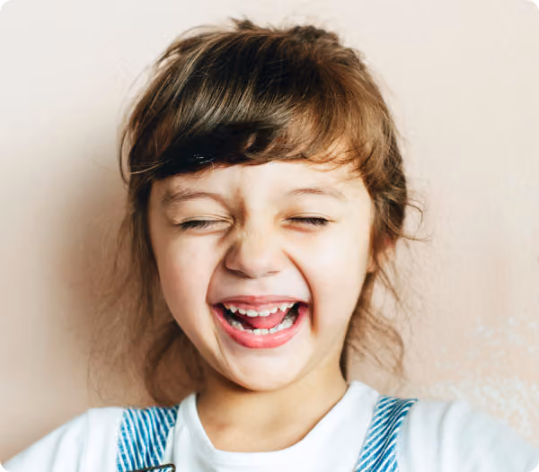 Young girl laughing widely with eyes closed, capturing the joy of healthy sleep.