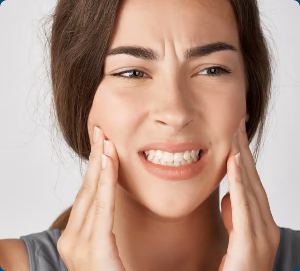 Woman touching her cheeks with both hands, displaying a pained expression that suggests jaw or facial discomfort.