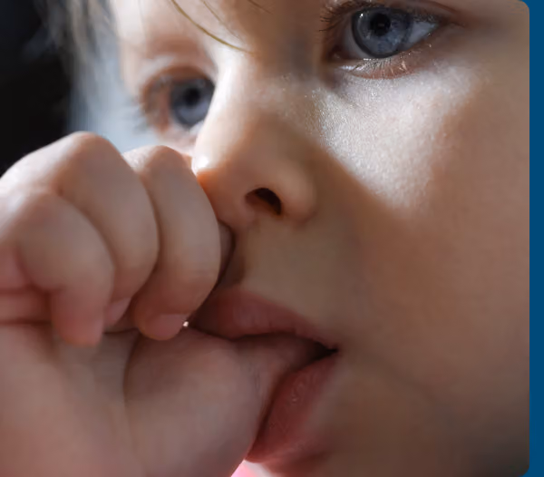 Young child holding a blue oral appliance while standing against a teal background.