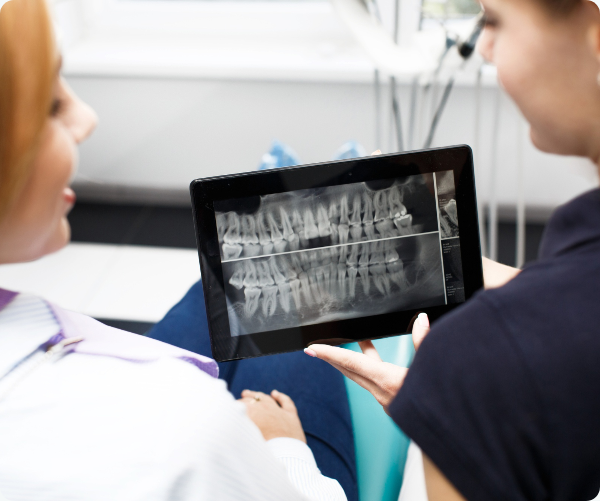 A dentist and patient review a panoramic dental X-ray on a tablet.