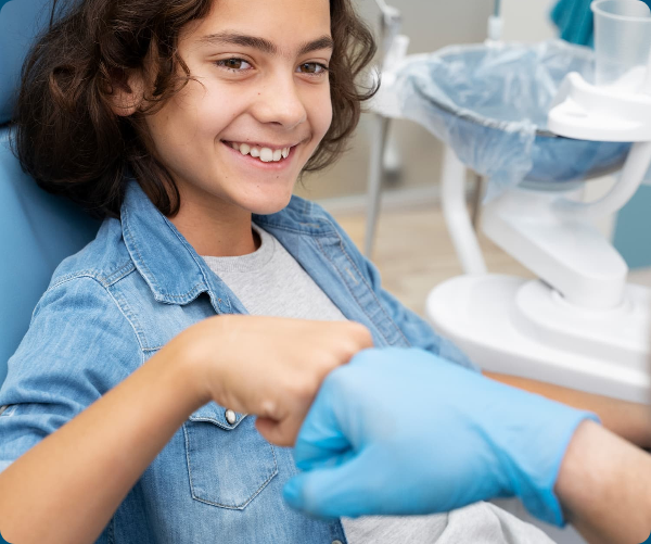 A child smiles from a dental chair while fist bumping a clinician in a dental office.