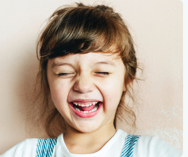 Young child laughing broadly against a pink background for early orthodontic care.