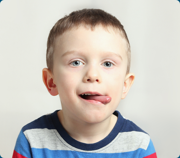 A young boy sticks out his tongue against a light background for myofunctional therapy.