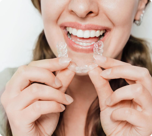 Smiling woman holding a clear retainer near her teeth.
