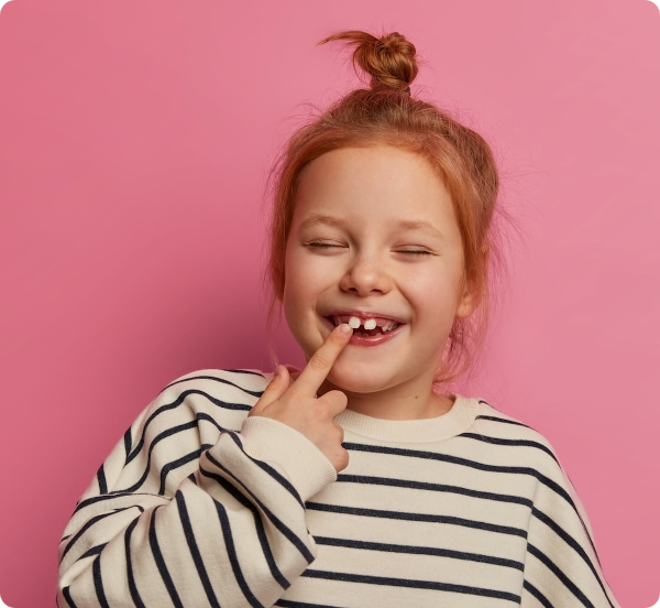 Smiling young girl with missing front teeth against a pink background.