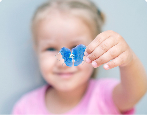 Young child holding a blue palate expander toward the camera.