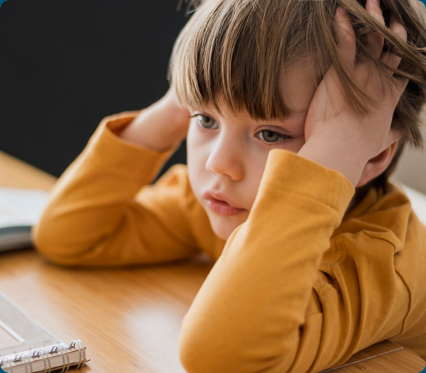 Young boy with hand on his head, looking distracted at a desk — tied to ADHD-like symptoms from poor sleep.