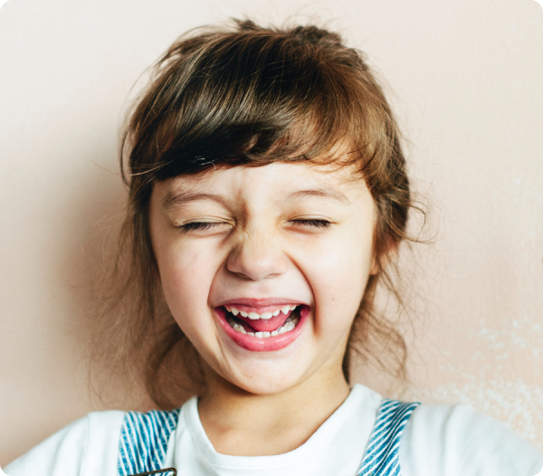 Young girl laughing widely with eyes closed, capturing the joy of healthy sleep.