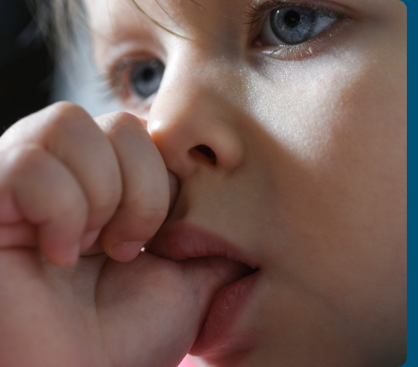 Young child holding a blue oral appliance while standing against a teal background.