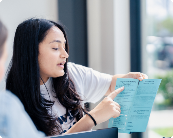 A young woman with long dark hair holds a printed brochure or guide, looking attentively as she reads the page.