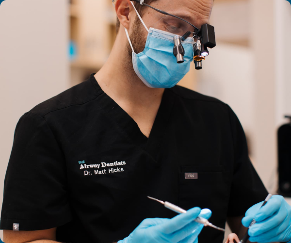 Dr. Matt Hicks of The Airway Dentists wearing a surgical mask and loupes, focused on dental work in a clinical setting.
