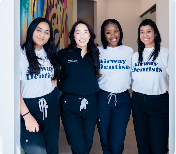 Four members of The Airway Dentists team standing in a doorway wearing matching white "Airway Dentists" tees and dark pants.
