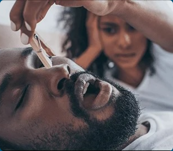 A clinician checks a sleeping patient’s airway while another person observes in the background.