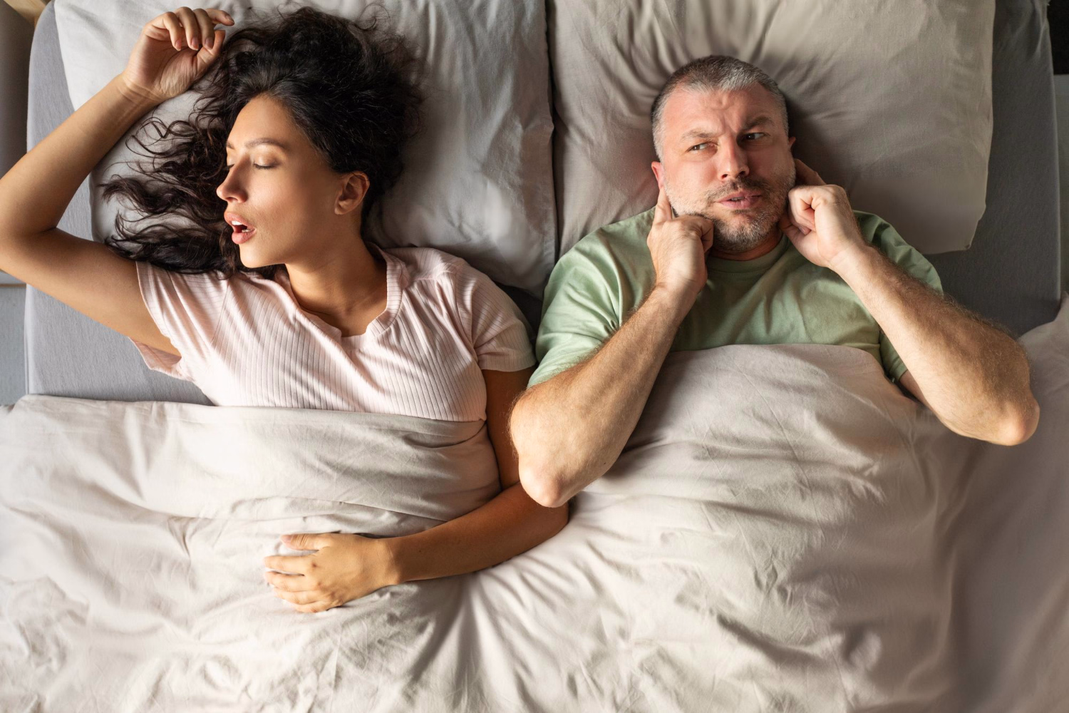 A man sleeps on his back with his mouth open, illustrating snoring and nighttime airway restriction.