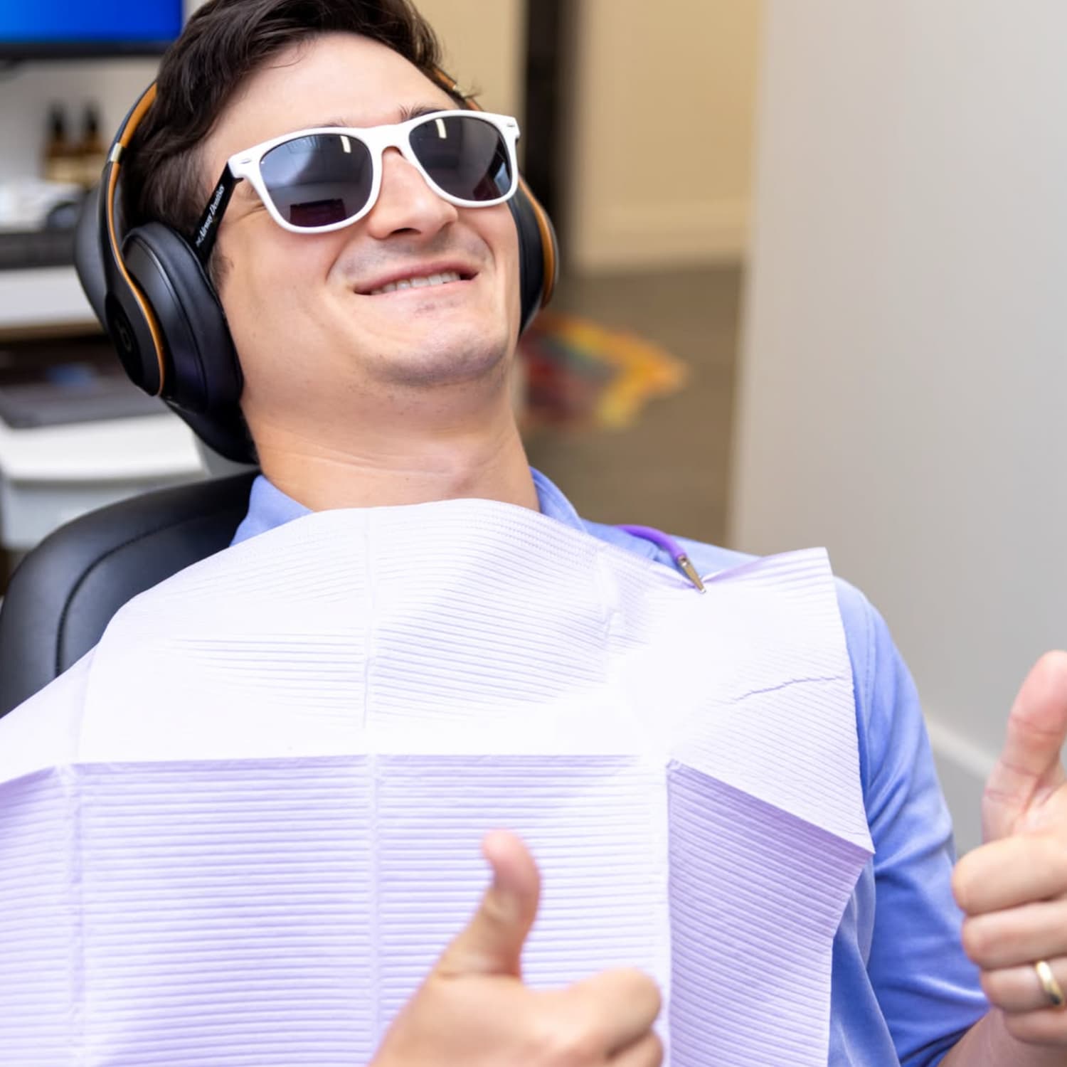 Adult male patient in a treatment chair, wearing sunglasses and giving a thumbs up