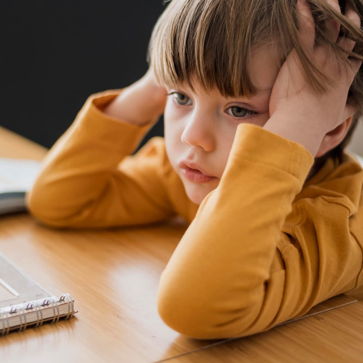 Young boy sitting at a school desk with his hands on his head, looking tired