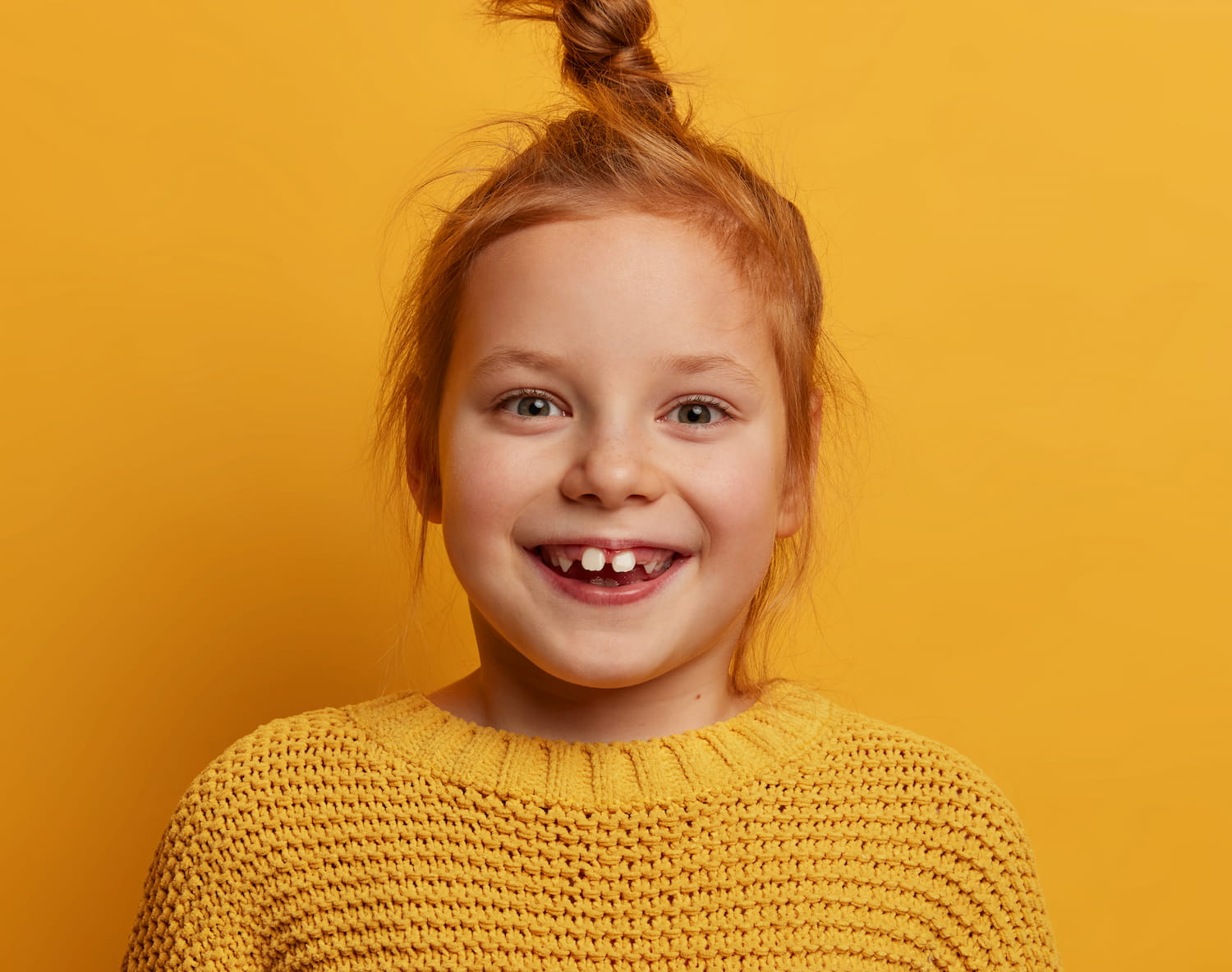 Smiling young girl in a yellow sweater against a yellow background