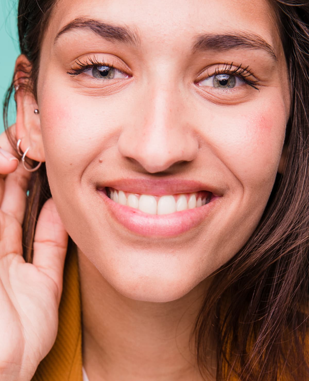 Smiling young woman with bright teeth, tucking her hair behind her ear