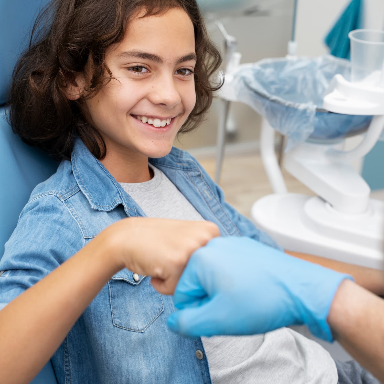 Pre-teen in a dentist’s chair, giving a fist bump to a gloved dentist’s hand