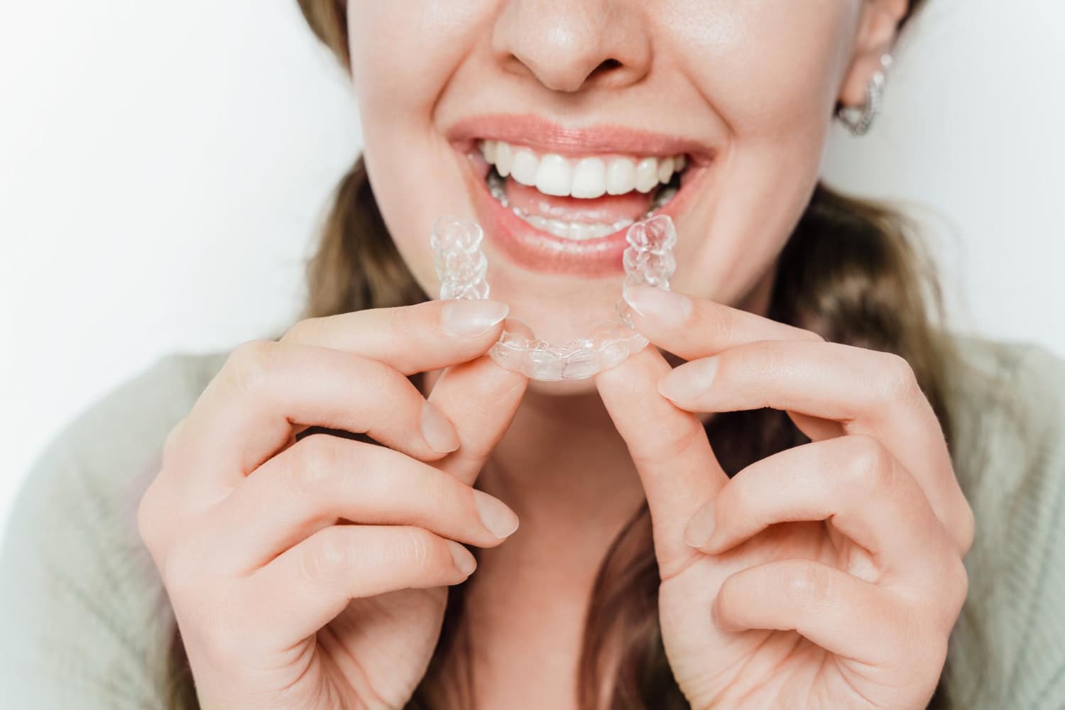 A person smiles while holding a clear dental aligner near their teeth, preparing to insert it into their mouth.