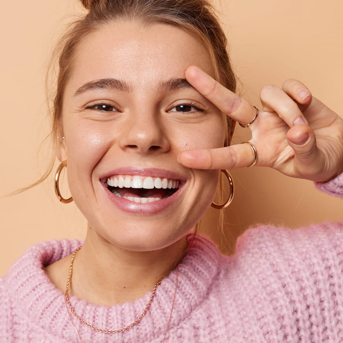 Happy young woman with big smile, making a peace sign with her hand