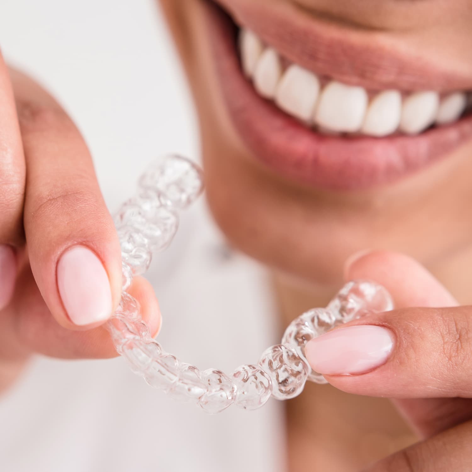 Smiling woman with straight teeth, holding an Invisalign® tray