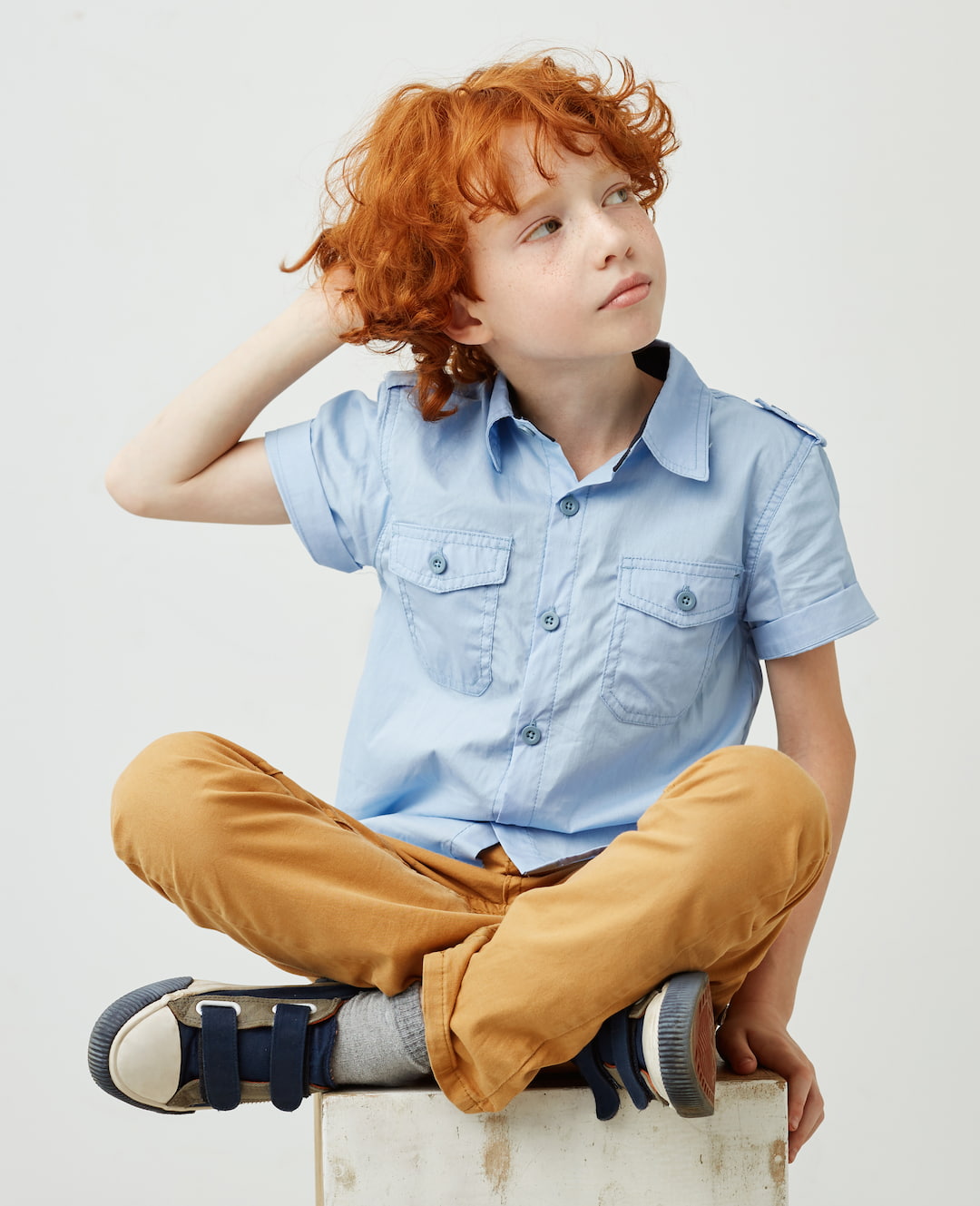 Boy sitting cross-legged on a stool, scratching his head in confusion