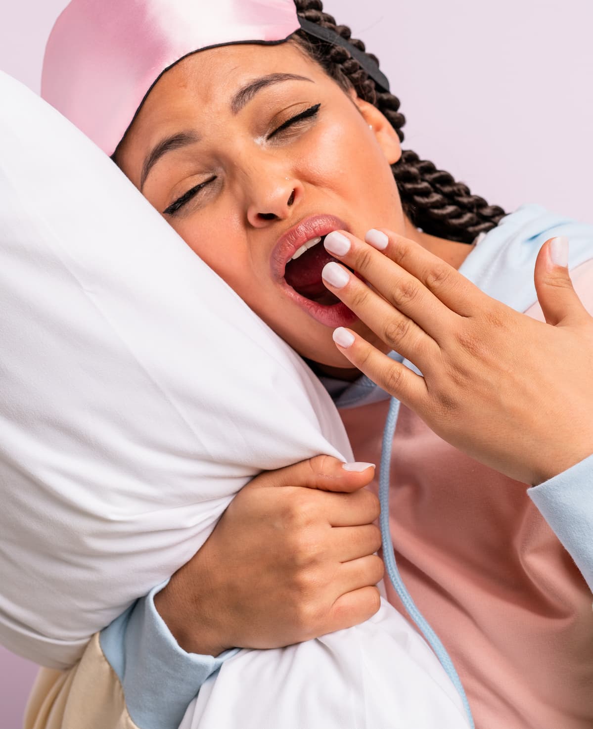 Woman hugging a pillow, yawning with her hand over her mouth