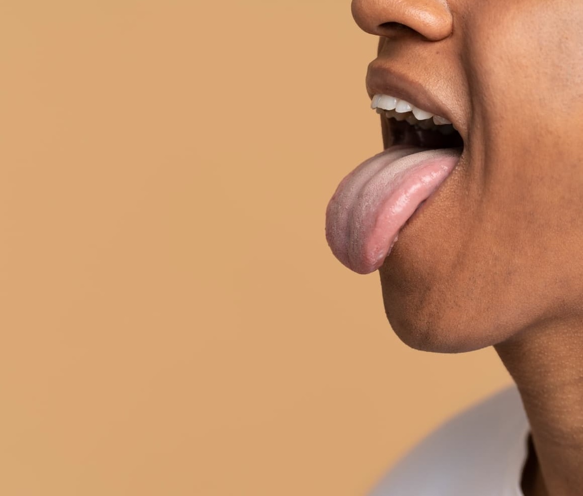 A person with medium-brown skin sticks out their tongue against a plain, light brown background.